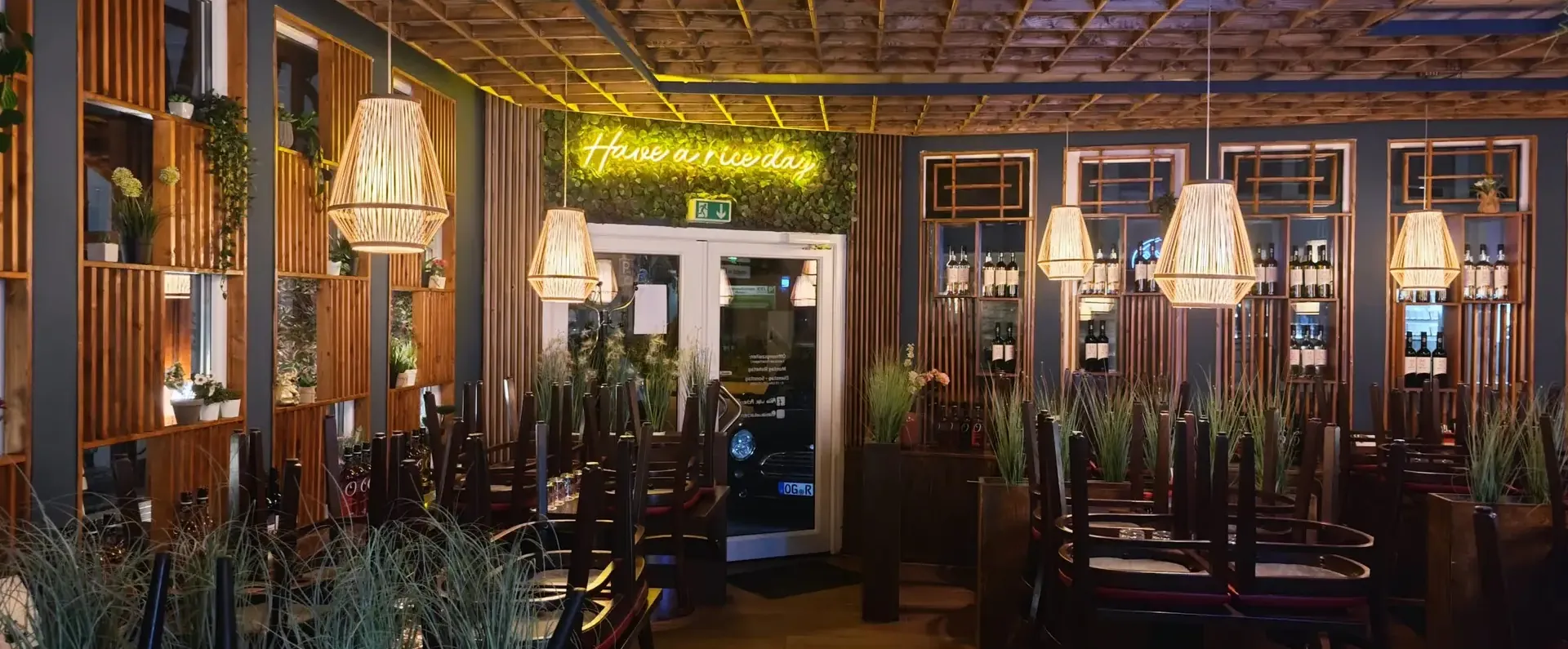 Gastraum des Asia Wok Achern am Abend, Bambuslampen und Neonschrift „Have a nice day“